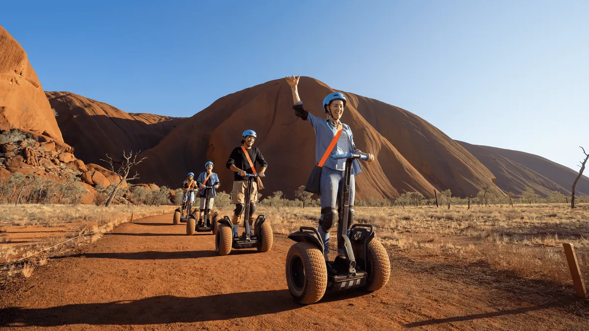 Riders on the Segway trail beside the sandstone wall on an Uluru base Segway tour at sunrise, Northern Territory Australia