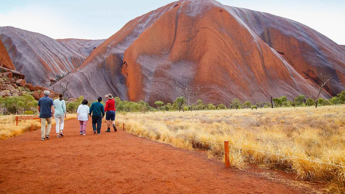 Walkers on the flat sand track beneath the rock face on a guided Uluru base walk at sunrise, Northern Territory Australia