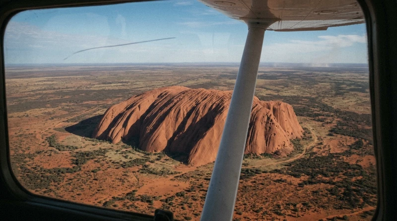 Fixed-wing aircraft wing over the red monolith and desert on a scenic plane flight Uluru tour, Northern Territory Australia